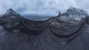 Drone view of sea waves washing coast with foamy water surrounded by snowy mountains under bright sky during sunset in