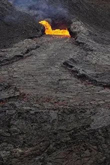 Drone view of stream of hot orange lava flowing through mountainous terrain in morning in Iceland