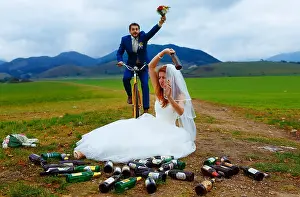 Throwing Prints: drunken bride with lots of empty beer bottles in mountain landscape and groom racing to her- funny wedding concept