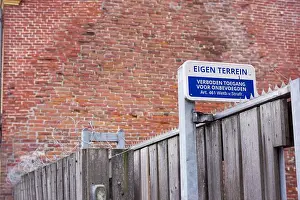 Prohibited Prints: Dutch blue private property sign with in the background a stone wall and a fence with barbed wire