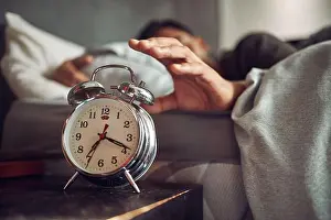 Exhausted Prints: Early to bed, early to rise. a young man reaching for his alarm clock after waking up in bed at home