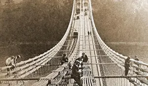 An early image showing workmen painting the Menai Suspension Bridge, Anglesey, Wales, UK without any safety gear