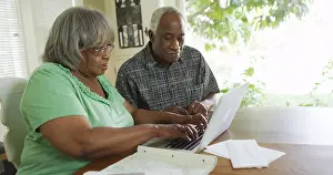 Elderly black woman typing on laptop with husband