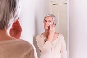At Home Prints: A elderly Caucasian women with short gray hair in casual clothes cares for the skin of the face