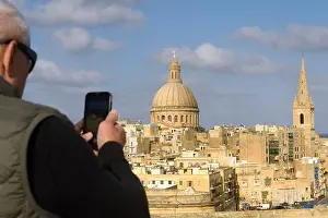 Historic Buildings Prints: An elderly gray-haired tourist in sunglasses takes photos with his phone from above