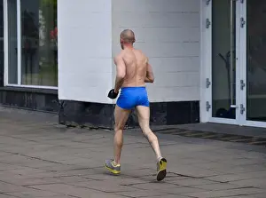 Elderly man in short shorts running cross country in the city in cold weather