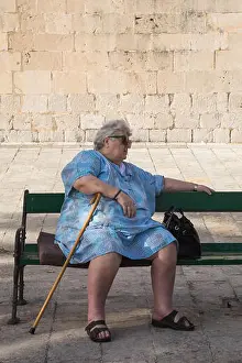 Balkan Prints: Elderly woman in blue dress with walking stick