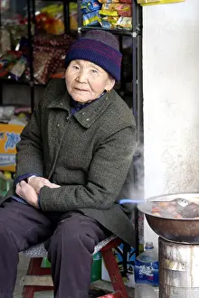 Senior Citizen Prints: elderly woman in a Hutong doorway selling hot food, Beijing, China