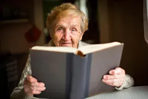 Grandma Prints: An elderly woman reading a big book sitting at a table in the house