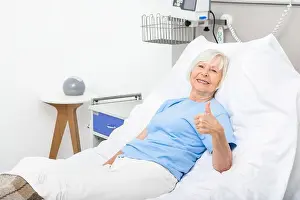 Ward Prints: Elderly woman showing thumbs up while lying in a hospital bed