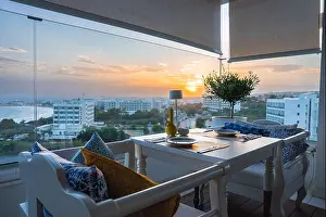Cushions Prints: Elegant Balcony Dining Setup Overlooking Coastal Cityscape at Sunset