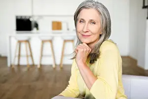 Contemplating Prints: Elegant charming middle-aged woman with gray hair sitting on the comfortable couch and looks at the camera