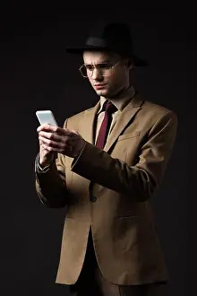 Formal Wear Prints: serious elegant man in beige suit, hat and eyeglasses using smartphone isolated on black