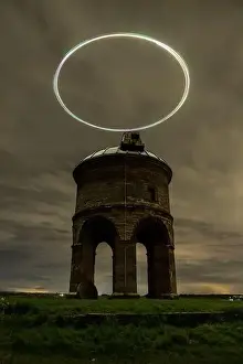 Enigmatic night view of an ancient windmill with a drone light trail creating a halo effect in the dark sky