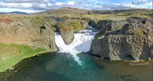 Epic aerial drone view flying over landscape of Hjalparfoss waterfall and lagoon on a sunny day