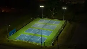 Evening aerial video of outdoor blue tennis courts with pickleball lines with lights turned on