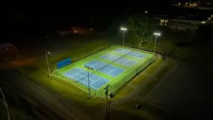 Blue Ball Prints: Evening aerial video of outdoor blue tennis courts with pickleball lines with lights turned