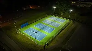 Evening aerial video of outdoor blue tennis courts with pickleball lines with lights turned on