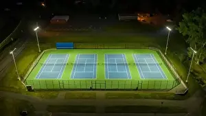 Evening aerial video of outdoor blue tennis courts with pickleball lines with lights turned on