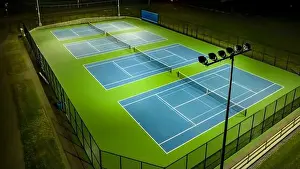 Evening aerial video of outdoor blue tennis courts with pickleball lines with lights turned on