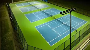 Evening aerial video of outdoor blue tennis courts with pickleball lines with lights turned on