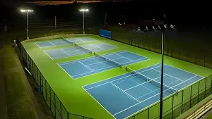 Evening aerial video of outdoor blue tennis courts with pickleball lines with lights turned on