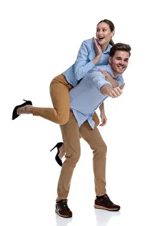excited casual woman looking surprisd while being carried by young man and looks to side, man is making the ok sign on white background