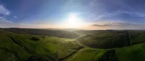 Green Valley Prints: An expansive drone shot captures the beauty of a green valley bathed in sunlight with undulating hills and clear skies