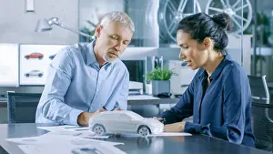 Prototype Prints: Experienced Automotive Designer and Female Engineer Works with Blueprints and Sketches of a New Car Prototype Model