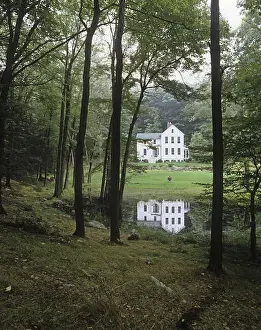 Vertical Image Prints: An exterior shot of a traditional country house painted white surrounded by forest and reflected in a small pond