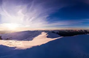 Fabulous evening panorama with snow-capped mountains and hills with bright sun and fog on a frosty winter evening
