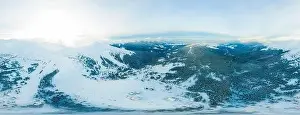 Fabulous evening panorama with snow-capped mountains and hills with bright sun and fog on a frosty winter evening