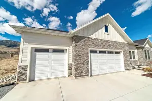 Attached Prints: Facade of home with gable roof white garage doors and stone wall against sky