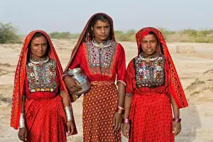 Three Fakirani women in traditional colorful clothes with a water jug, Great Rann of Kutch, Gujarat, India