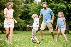 Family and kids play soccer together at garden in summer