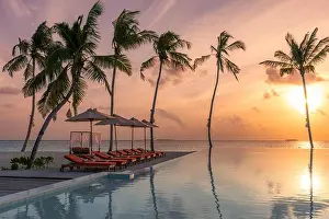 Fantastic poolside, sunset sky, palm trees reflection. Luxury tropical beach landscape, infinity swimming pool, deck chairs bed under umbrellas