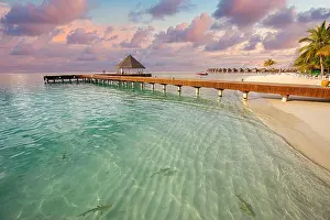 Fantastic sunset beach shore, shallows with sting rays and sharks in Maldives islands. Luxury resort hotel, wooden jetty, over water villa, bungalow