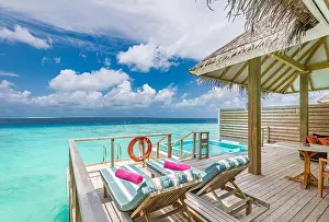 Fantastic over water villa, terrace view with sun beds chairs under umbrella, luxury pool hotel with stunning ocean view. Beautiful spa or wellness