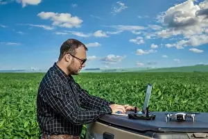 Farmer standing in soybean field looking at notebook and drone