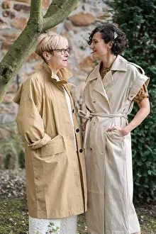Curly Hair Prints: Two fashion women in stylish beige trench coats share a joyful moment outdoors