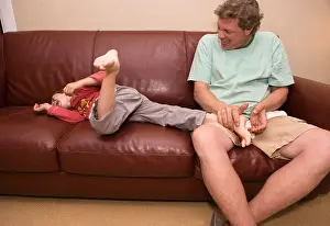 father tickling five year old son at home on couch