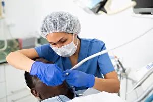 Dentistry Prints: Female dentist performing teeth treatment to adult man at clinic
