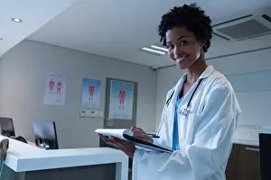 African Ethnicity Prints: Female doctor looking at camera while writing on clipboard in the hospital
