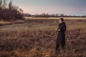 Remote Controller Prints: Female drone pilot looks at drone while operating in a field during autumn at dusk