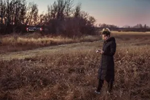 Remote Controller Prints: Female drone pilot looks at her remote controller while operating in a field during autumn at dusk