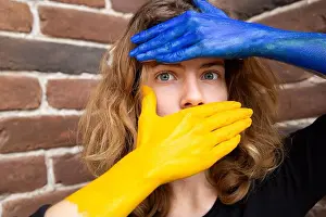 Unrecognizable Prints: female eyes, piercing gaze, face covered with hands painted in the colors of the Ukrainian flag