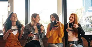 Gossip Prints: Female friends sitting in cafe holding a cup of coffee and smiling