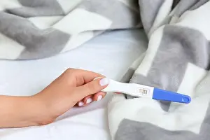 Hormone Prints: Female hand with positive pregnancy test and plaid on bed, closeup