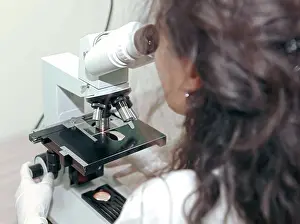 Analyzing Prints: Female lab technician analyzing sample through microscope