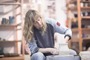 Shaping Prints: Female potter forming clay pot on pottery wheel in workshop
